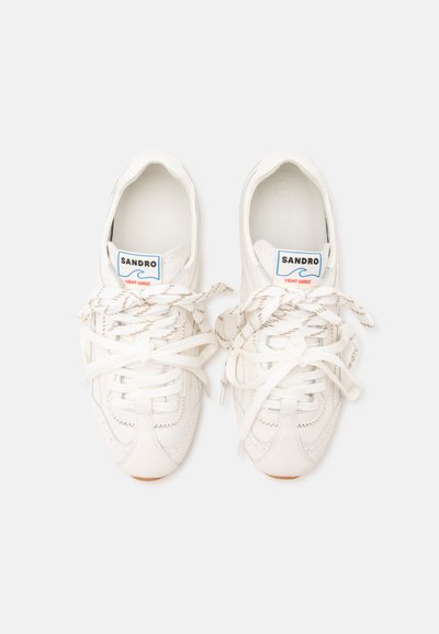 Baskets en cuir blanc avec lacets beiges à rayures noués lâchement, étiquette de marque "Sandro Light Wave" visible sur la languette, vues de dessus sur fond blanc.