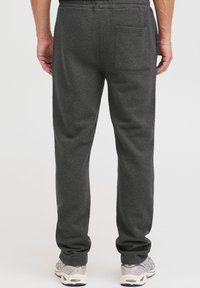 Gray sweatpants made of soft cotton blend fabric, featuring a single back pocket and elastic waistband. Paired with light gray sneakers.