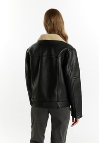 Giacca in pelle nera con colletto in shearling crema, texture liscia e vestibilità comoda. Presenta chiusure a bottone e tasche laterali.