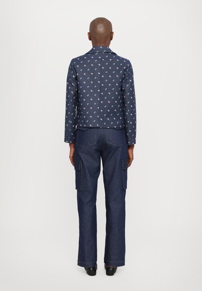 Jachetă din denim albastru cu un model floral, asociată cu blugi cargo cu picioare largi. Hainele au detalii cu buzunare și cusături contrastante.