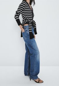 Pasiasty czarno-biały kardigan związany w talii, noszony na wysokich niebieskich szerokich dżinsach, w połączeniu z czarnymi sandałami na obcasie.