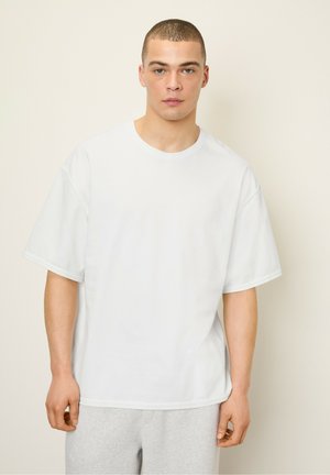 White oversized t-shirt made of cotton, featuring short sleeves and a crew neck. Smooth texture with minimal stitching detail.