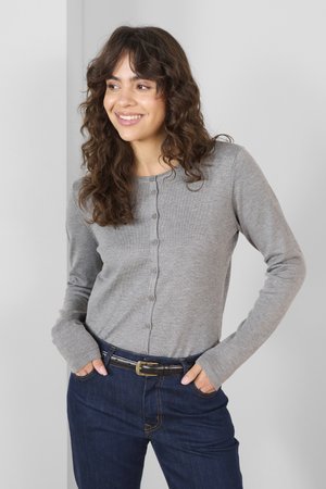 Hellgrauer Cardigan mit langen Ärmeln und Knöpfen auf der Vorderseite, getragen über einer dunkelblauen Jeans, mit weicher Textur und gerippten Bündchen.
