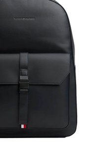 Zaino sintetico nero con texture liscia, chiusura a patta assicurata da una cinghia con fibbia, caratterizzato da un piccolo accento logo rosso, bianco e blu.