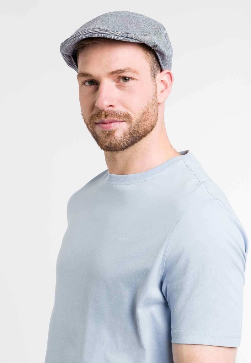 Casquette plate grise à texture légère, avec des rayures subtiles et un bord incurvé. Portée avec une chemise à manches courtes bleu clair.