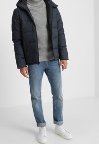 Dark blue puffer jacket with a hood, worn over a light grey ribbed sweater, paired with light blue jeans and white sneakers.
