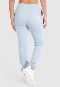 Helle blaue Sweatpants aus weichem Stoff; mit einem elastischen Bund, seitlichen Taschen und engen Knöchellöchern. Kombiniert mit weißen Sneakers.