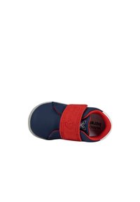 Zapato infantil de color azul marino con una tira de velcro roja. Presenta una superficie texturizada, punta redondeada y una suela blanca en contraste.