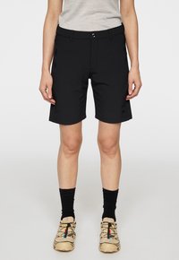 Mustat shortsit, jotka on valmistettu kevyestä materiaalista, suoran leikkuun omaavat, vyölenkit ja vetoketjulliset taskut. Yhdistetty beigen värisiin kenkiin ja mustiin sukkiin.