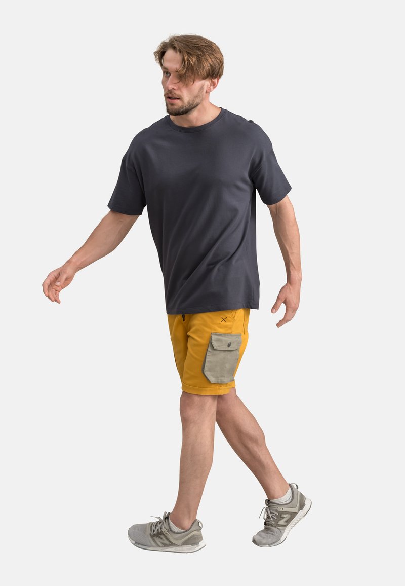 T-shirt grigio scuro, pantaloni corti gialli con una tasca a toppa grigia chiara e sneaker grigie. Design semplice, vestibilità casual e materiale leggero.