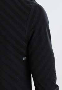 Mustapaita pitkillä hihoilla, jossa on tekstuuripinta ja vinot raidat. Hihassa on pieni harmaa "D1" -merkki.