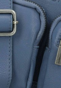Borsa in pelle blu con una texture liscia, accessori metallici e cuciture a contrasto. Include compartimenti con zip per la conservazione.