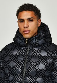 Puffer jacket in glossy black with a geometric embossed pattern. Features a zip closure and a padded hood for added warmth.