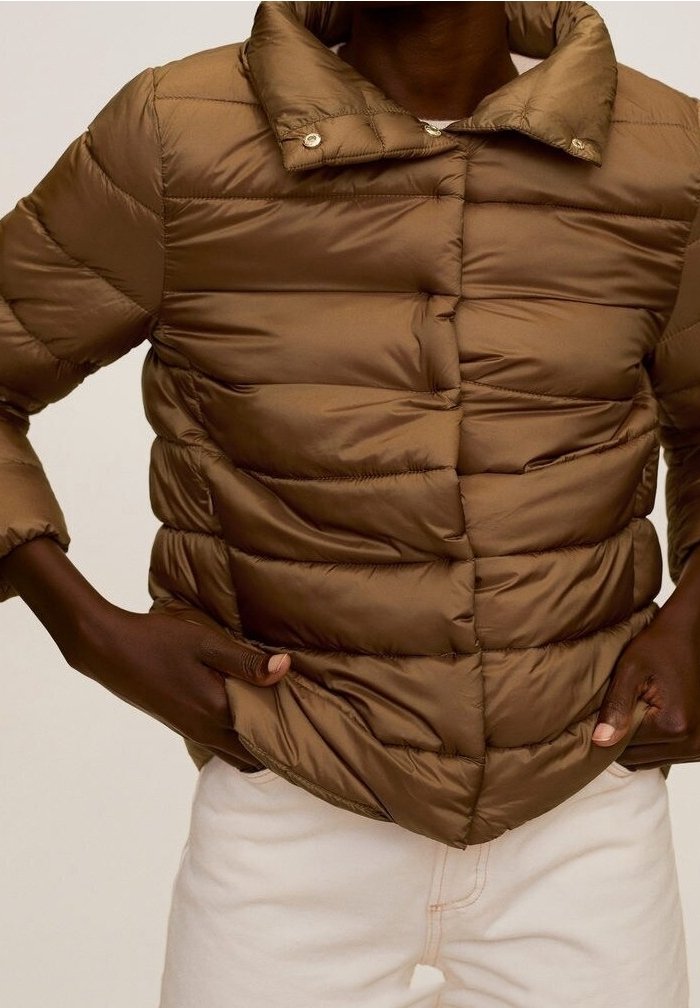 Doudoune marron matelassée avec boutons-pression portée par une personne ajustant l'ourlet, associée à un pantalon de couleur claire.