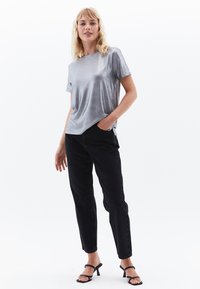 Camiseta corta de manga corta de color plata metálico con un ajuste relajado, combinada con jeans negros ajustados y sandalias de tacón negras. Textura suave y diseño minimalista.