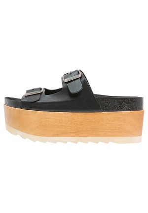 Sandalia de plataforma de piel negra con dos hebillas ajustables, base de madera y suela de goma texturizada. Presenta una entresuela gruesa y contorneada.