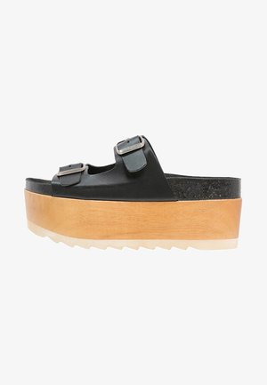 Sandale plateforme en cuir noir avec deux boucles réglables, base en bois et semelle en caoutchouc texturée. Présente un épais intermédiaire moulé.