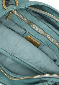 Interno della borsa in pelle color turchese con più scomparti con zip e una placca con logo dorato. Texture liscia con dettagli di cucitura discreti.