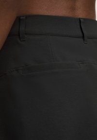 Pantalones cortos negros con una textura de tela suave, cinturilla ajustada y un único bolsillo trasero con diseño plano.