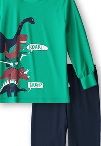 Groene langarmshirt met dinosaurustekeningen en tekst "ROAR!" en "GRRRRR." Gecombineerd met donkerblauwe broek, beide van zachte stof.