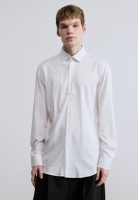 Λευκό πουκάμισο με κουμπιά, μακρυμάνικο, με κλασικό γιακά, απαλό ύφασμα και ίσια γραμμή. Διαθέτει κλείσιμο με κουμπιά μπροστά και μανίκια με μανσέτες.