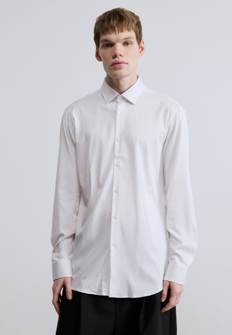 Λευκό πουκάμισο με κουμπιά, μακρυμάνικο, με κλασικό γιακά, απαλό ύφασμα και ίσια γραμμή. Διαθέτει κλείσιμο με κουμπιά μπροστά και μανίκια με μανσέτες.