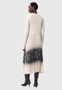 Maglione lavorato a maglia color crema con maniche lunghe abbinato a una gonna midi plissettata con un motivo a stampa serpente bianco e nero, e stivali con tacco alto.