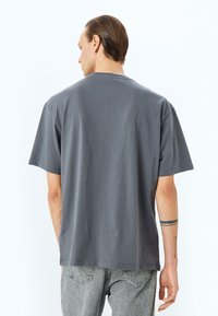 Camiseta gris de manga corta con un corte relajado, hecha de tela suave. Presenta un cuello redondo y un diseño minimalista, mostrada desde la parte de atrás.
