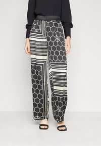 Pantalon large à motifs noirs et blancs comprenant des formes hexagonales et des rayures, avec une ceinture en satin lisse et une coupe décontractée.