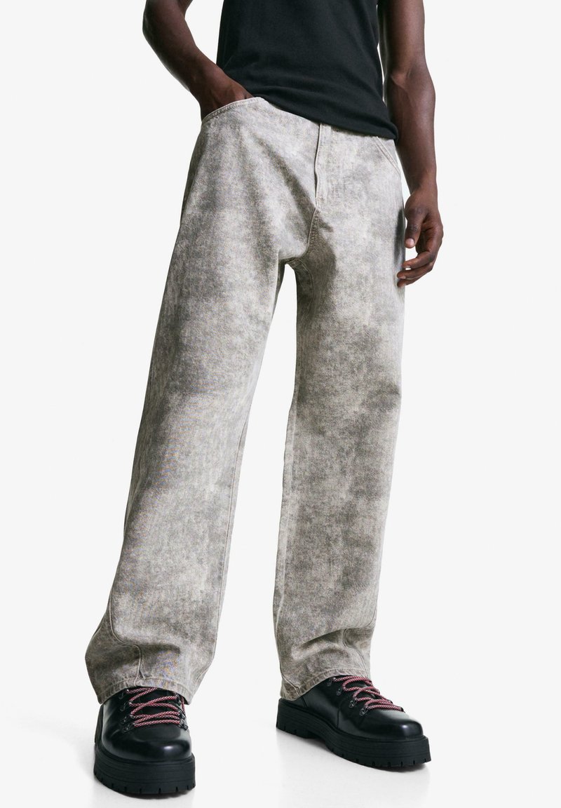 Helle graue weite Jeans aus weichem, strukturiertem Stoff mit ausgewaschenem Finish, versehen mit Fronttaschen und detailreicher Naht. Kombiniert mit schwarzen Stiefeln.