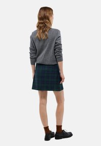 Pull en tricot gris, jupe à carreaux verte et marine, courte, texture lisse. Complété par des chaussures noires et des chaussettes marron.