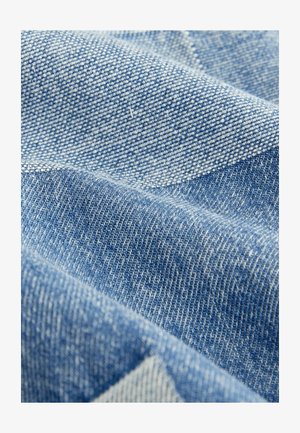 Țesătură din denim albastru cu o țesătură texturată. Variatiile de nuanță creează un model de lumini și umbre, evidențiind finețea și durabilitatea sa.