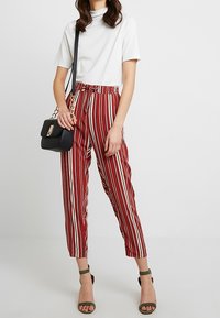 Pantalon rayé rouge et blanc avec une taille élastique, associé à un haut blanc uni et un sac bandoulière noir. Sandales vertes à talons larges.
