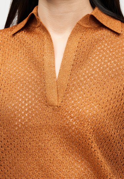 Κοντινή λήψη ενός ατόμου που φοράει πορτοκαλί, υφασμάτινο πλεκτό τοπ με γιακά και V-σχήμα λαιμόκοψη.