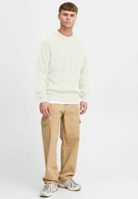 Lys grønn ribbestrikket genser med rund hals, kombinert med beige cargo-bukser med sidelommer og grå joggesko.