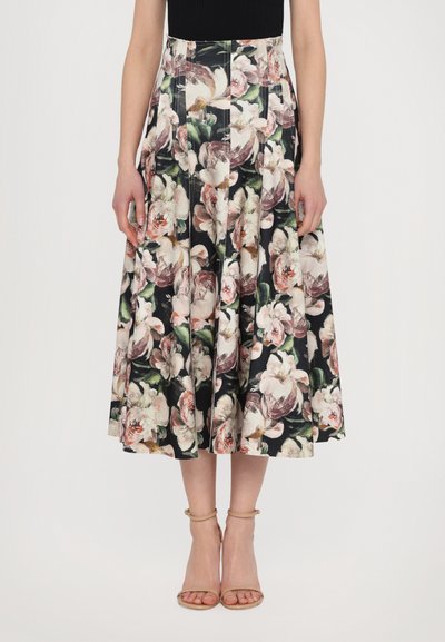 Jupe midi florale noire, ornée de grandes fleurs roses et blanches, avec un design plissé et une taille cintrée, associée à des talons nus à bride de cheville.