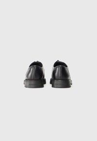 Zapatos de cuero negro con un acabado suave, punta redondeada y suela de goma baja. La marca está grabada en el talón.
