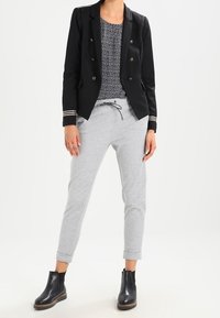 Svart dubbelknäppt kavaj med guldknappar, vit topp med prickar, grå tapered joggers och svarta ankelskor med träklack.