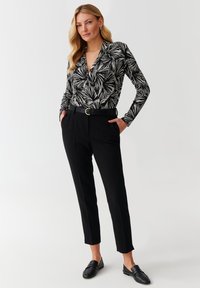 Blusa de patrón en blanco y negro con mangas largas y escote en V, combinada con pantalones negros de cintura alta y mocasines negros. Cinturón con hebilla redonda.