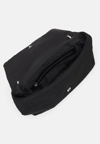 Sac en bandoulière noir Calvin Klein ouvert pour montrer une poche zippée intérieure avec un revêtement de marque et un fermoir magnétique argenté sur fond uni.