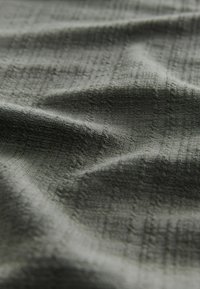 Textureret stof i mørkegrøn med et gitterlignende mønster, der har subtile variationer i overfladedybde og blødhed.