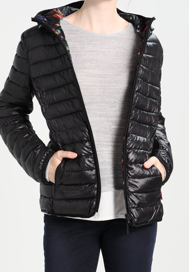 Veste matelassée noire avec une texture matelassée verticale, fermeture éclair frontale et deux poches latérales ; doublure à motifs visible à l'ouverture de la capuche.