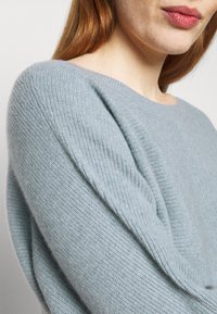 Jasnoniebieski sweter dziany z okrągłym dekoltem i opuszczonymi ramionami, charakteryzujący się miękką fakturą i prążkowanymi detalami na rękawach.