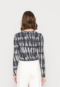 Top corto a maniche lunghe in un tessuto grigio scuro con un motivo tie-dye bianco. Presenta un collo rotondo e una silhouette aderente.