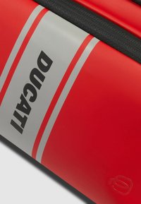 Equipaje rojo de Ducati con una textura suave, franjas grises y letras negras en negrita. Incluye cremallera negra contrastante y detalle del logo.