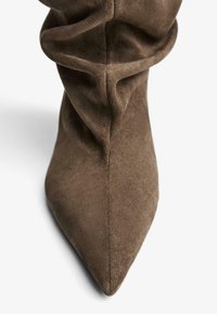 Stivale alla caviglia in camoscio marrone con punta appuntita e dettagli arricciati sul gambale, che mostrano una texture morbida e una finitura liscia.