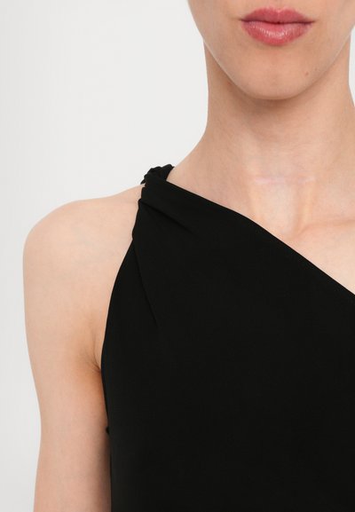 Top sans manches noir avec un col torsadé, texture lisse et coupe ajustée, mettant en valeur les épaules et la clavicule.
