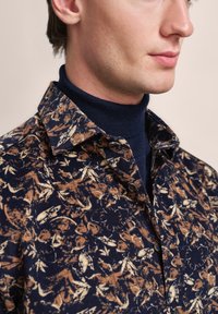 Marineblaues Hemd mit einem abstrahierten beigen Blumenmuster, das über einen klassischen Kragen, Knopfdetails und einen strukturierten Stoff verfügt.