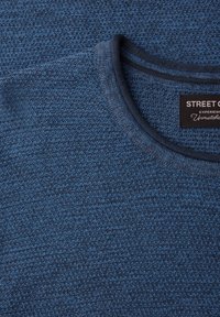 Jersey azul de punto con cuello redondo, tejido texturizado y una etiqueta con la marca "STREET G" en el interior del cuello.