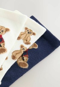 Drei Paar Socken: ein cremefarbiges Paar mit Bärendesign, ein marineblaues Paar mit Bär sowie ein strukturiertes Strickpaar in Dunkelblau. Jedes Paar hat Plüschbärenakzenten.